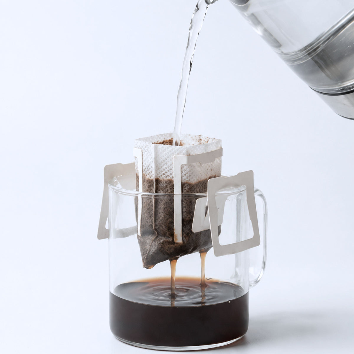 Hot water poured from a kettle into a KNDZ drip bag hanging on a glass mug